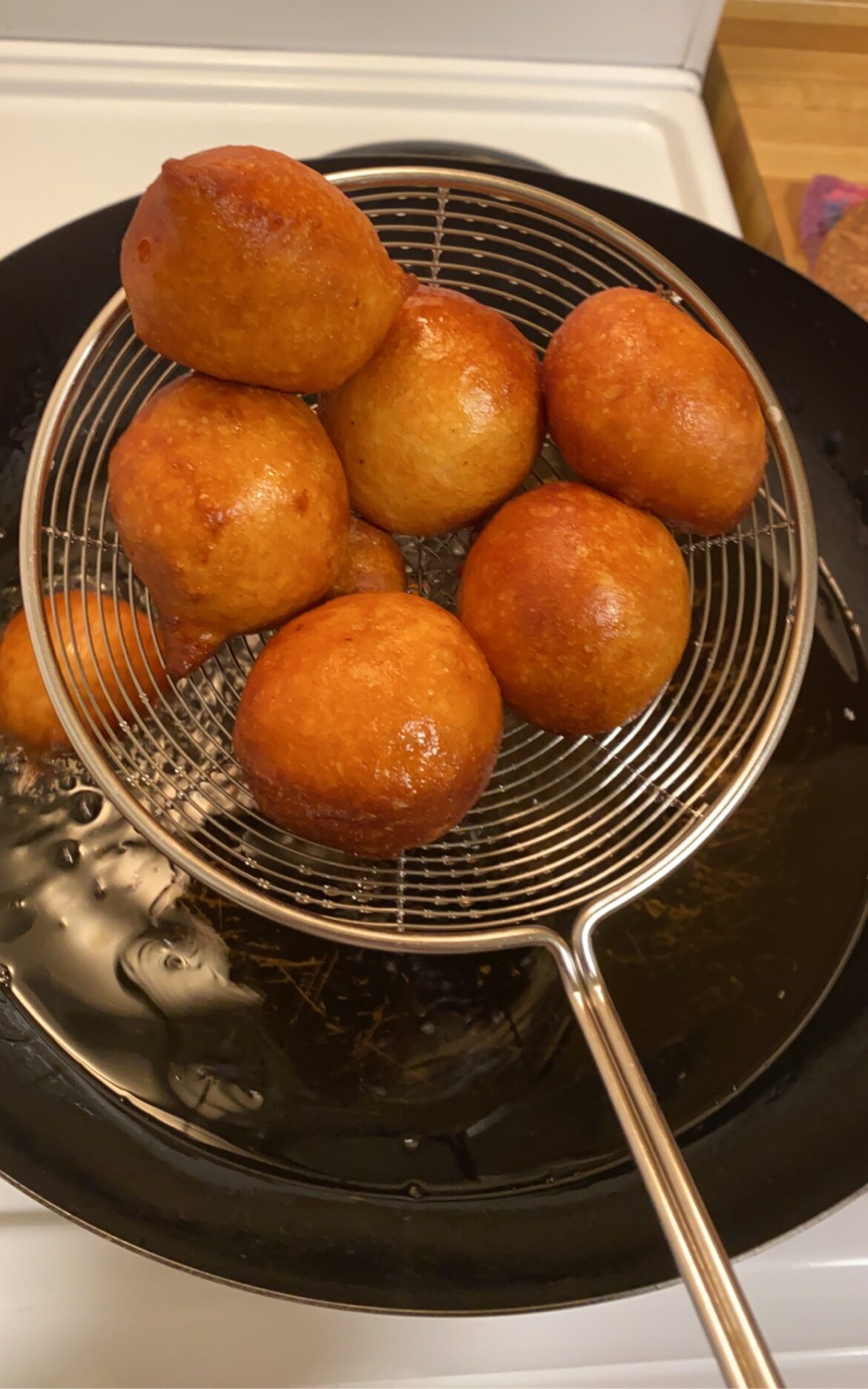 Freshly fried puff puff been scooped using a spider spoon from the hot oil.